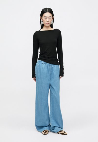 Melna garām piedurknēm blūze, kombinēta ar gaiši zilām platām kājām džinsiem un leoparda raksta mūlēm. Vienkāršs dizains ar brīvu piegriezumu un mīkstu tekstūru.