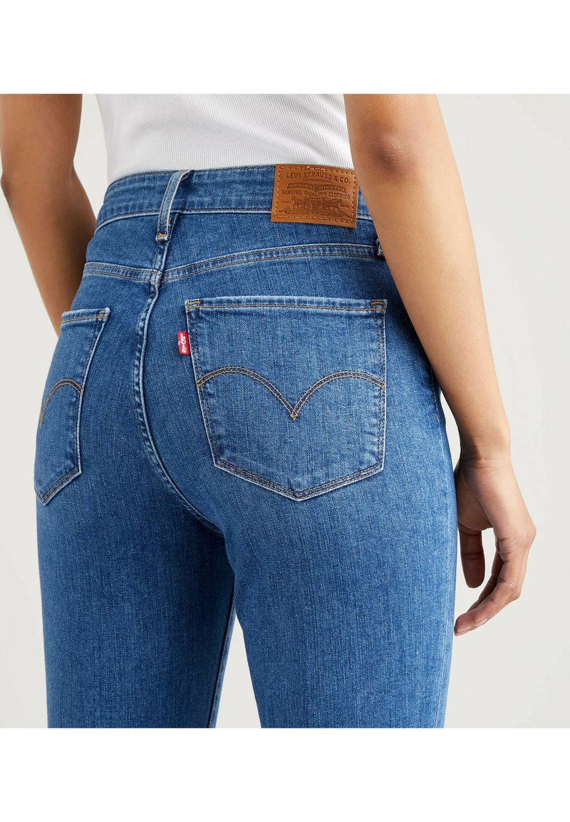 Blaue Jeans aus Denim mit mittelhohem Bund, ausgestattet mit klassischen Gesäßtaschen und einem braunen Leder-Label-Patch am Bund.