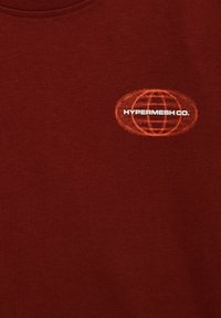 Tissu bordeaux avec un petit motif de globe orange et le texte blanc "HYPERMESH CO." sur la zone de la poitrine d'un vêtement.