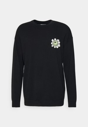 Sudadera negra con cuello redondo y mangas largas. En el lado izquierdo del pecho tiene un diseño bordado de una flor con una cara sonriente.