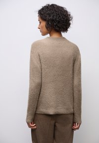 Beige neulotun villapaita, jossa on pehmeä, teksturoitu pinta, pitkät hihat ja pyöreä kaula-aukko, yhdistettynä yhteensopiviin ruskeisiin housuihin.