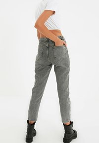 Jeans gris taille haute avec une coupe droite, dotés de poches arrière et de coutures visibles. Portés avec un t-shirt court blanc et des bottes noires.