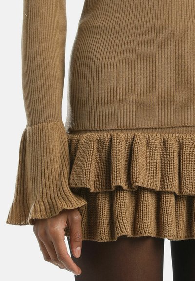 Ribota brūna džemperis ar izplestām piedurknēm un viļņotu apakšmalu. Tekstūras adījuma audums, pieguļošs augšdaļa un kārtota viļņotā detaļa apakšā.