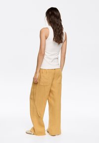 White sleeveless top paired with loose, mustard-yellow linen pants featuring two back pockets and frayed hem edges.