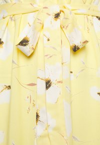 Tessuto giallo con un motivo floreale che presenta fiori bianchi e accenti marroni. Include una cintura coordinata e dettagli plissettati.