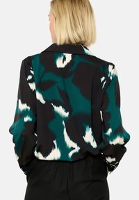 Long-sleeve blouse in black with a teal and white abstract pattern. Features a collared neckline and buttoned cuffs. Smooth, lightweight fabric.