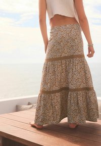 Maxi-jurk in een bloemenprint met bruine en beige tinten, voorzien van gelaagde lagen en een getextureerde zoom, gedragen met een cropped top.