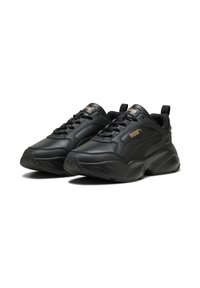 Schwarze Sportschuhe aus synthetischem Leder mit einer dicken Sohle, die auffällige Markierung und strukturierte Einsätze auf dem Obermaterial aufweisen.
