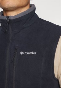 Navy fleece vest with gray collar, zippered front, and Columbia logo. Features smooth texture and a fitted design, ideal for layering.