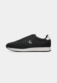 Black athletic shoes with a smooth fabric upper, white accents on the heel, and a thick white sole featuring a textured pattern. Logo on side.
