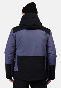 Herrenjacke in Lila- und Schwarztönen, mit Kapuze, verstärkten Nähten und geprägtem Logo auf dem oberen Rücken. Wasserdichtes Material.
