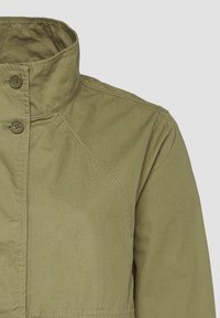 Veste légère vert olive avec un col haut, fermeture à deux boutons et de subtils détails de coutures aux épaules. Tissu lisse.