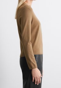 Maglione in maglia marrone chiaro con maniche lunghe, scollo a giro, polsini e orlo a coste. Abbinato a pantaloni in pelle nera.