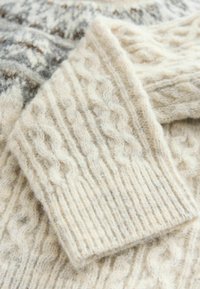 Cremfarbener gestrickter Pullover mit Kabelstrickmuster und gerippten Bündchen, aus weicher Wolle mit einem leicht flauschigen Aussehen.