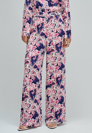 Mujer con pantalones de cintura alta y pierna ancha con estampado de remolinos florales en azul, rosa y blanco, combinados con un top de manga larga a juego.