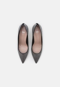 Talons aiguilles à bout pointu avec un motif métallique noir et argent, présentant un intérieur beige lisse et un contour noir le long du bord supérieur.