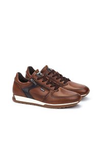 Sneaker in pelle marrone con accenti neri, texture liscia, design con lacci e suola in gomma bianca. Presenta una cerniera laterale per facilitarne l'uso.