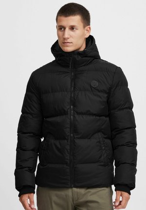 Black puffer jacket with a high collar and attached hood. Features quilted design, side pockets, and a circular logo on the chest.