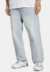 Jasnoniebieskie dżinsy o luźnym kroju, z widocznym przeszyciem, bocznymi kieszeniami i postrzępionymi krawędziami. W połączeniu z białymi butami sportowymi.