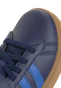 Zapato de cuero marino con rayas azules, área de cordones texturizada y suela de goma marrón claro. Punta redondeada y detalles de costura en la parte superior.