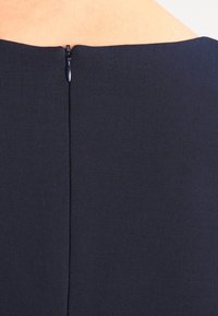 Robe marine avec une texture lisse, présentée avec une fermeture éclair cachée à l'arrière et un design épuré et ajusté.