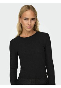 Svart ribbad långärmad topp med rund halsringning och mjuk struktur, med en något cropped nederdel och subtila fransdetaljer.