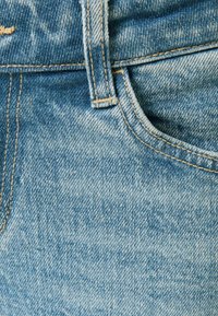 Tejido de denim azul con un lavado desvanecido, con costuras dobles, una cinturilla y un contorno de bolsillo frontal visible.