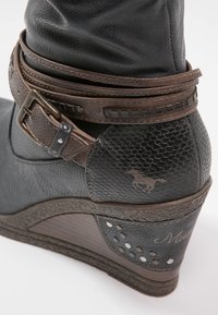Stivaletto con tacco a wedge in pelle nera con finitura texurizzata, fascia in pelle marrone, dettagli metallici, logo a forma di cavallo e lati perforati.