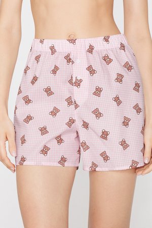 Pantalones cortos rosas a cuadros con estampado de pequeños ositos marrones, usados por una persona mostrada desde la cintura hasta la mitad del muslo.