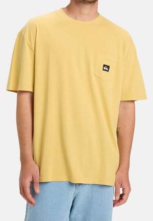 Camiseta de algodón amarilla con un ajuste cómodo, mangas cortas y un bolsillo en el pecho izquierdo que presenta un pequeño parche de logo negro.