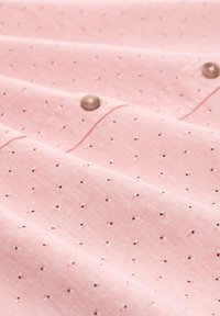 Helles rosa Stoff mit kleinen, gleichmäßig verteilten schwarzen und weißen Punkten. Hat eine glatte Textur und ein Detail mit Knopf.
