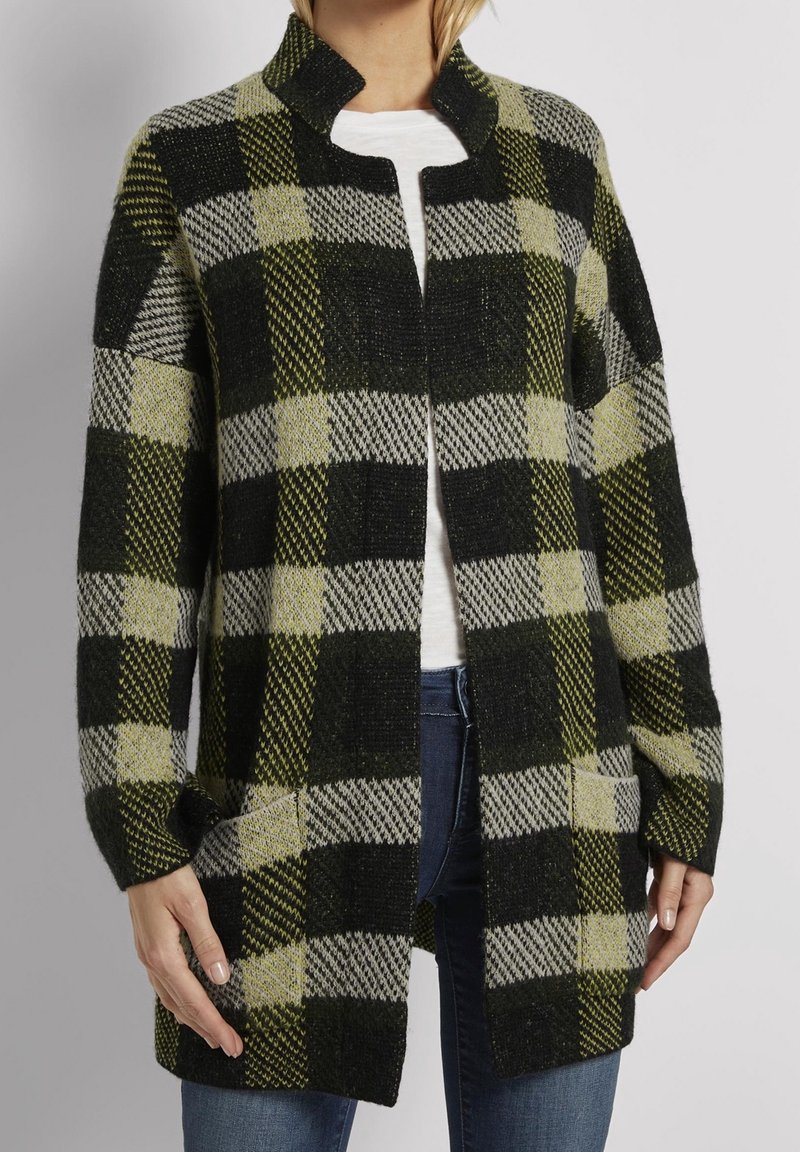 Zeleno-černý kostkovaný kardigan s vysokým límcem, otevřeným předním dílem a kapsami. Vyroben z texturované tkaniny, s kostkovanými vzory v různých velikostech.
