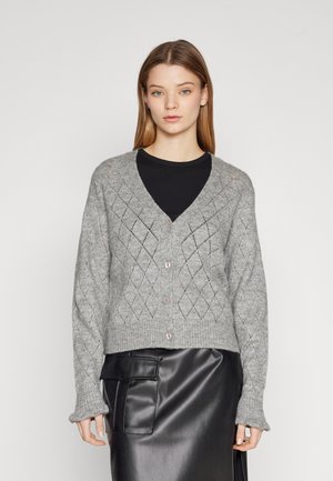 Grå strikket cardigan med diamantmønster, ribbet hem og knappelukking foran. Kombinert med et sort skinnskjørt. Teksturert stoff.