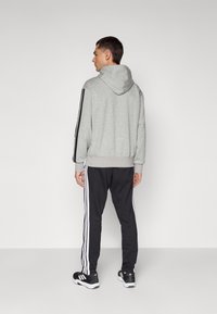 Grey hoodie with a drawstring, black side stripes, paired with black sweatpants featuring three white stripes on the sides. Black athletic shoes.