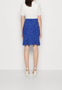 Gonna a fiori blu con orlo arricciato, vita arricciata e top bianco con maniche a sbuffo corte, abbinata a scarpe con tacco alte color crema.