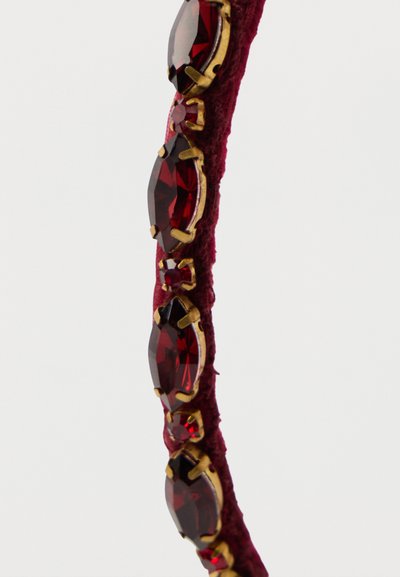 Čelenka s červenými drahokamami s oválnymi a okrúhlymi karmínovými kameňmi, osadená v kovovom prevedení zlatej farby, pripevnená na textúrovanom bordovom textilnom páse.