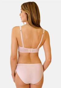 Jasnoróżowy biustonosz bezprzewodowy z regulowanymi ramiączkami, zapięciem na haftki z tyłu oraz miękką fakturą. Widoczne są również dopasowane majtki bezszwowe.