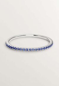 Pulsera de brazalete de plata que presenta una fila de piedras preciosas azules, forma circular, acabado suave y monturas de piedra ligeramente elevadas.