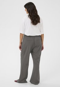 Pantalons gris à jambes larges avec une coupe décontractée, dotés d'une taille à cordon de serrage et de deux poches arrière. Associés à un t-shirt blanc ample.