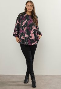 Blusa nera floreale con motivi rosa e viola, maniche lunghe, collo rotondo e dettagli in pizzo. Abbinata a pantaloni skinny neri e ankle boots.