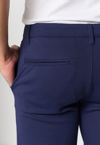Dark blue stretch fabric pants with a smooth texture, featuring a back pocket and a fitted waist design. Casual style with a clean finish.