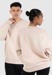 Sweat-shirt rose clair avec des poignets et un col côtelés, comportant un grand graphique "LOD" ton sur ton au dos. Tissu doux et texturé.