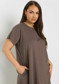 Luftiges, kurzärmeliges Kleid aus muted braunem Stoff. Hat Seitentaschen und dezente Nahtdetails für zusätzliche Textur.