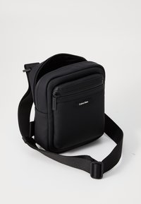 Borsa a tracolla nera realizzata in materiale morbido e testurizzato. Presenta un compartimento principale con zip e una piccola tasca frontale. Include una tracolla regolabile.