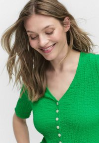 Green textured top with a v-neckline and short sleeves. Features several white buttons down the front.