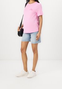 Růžové bavlněné tričko s krátkými rukávy a malým logem. Spárované se světle modrými džínovými šortkami a bílými teniskami. Černá kabelka přes rameno.