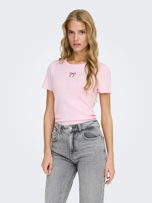 Young woman with long blonde hair wearing a light pink short-sleeve shirt with a small bow design and high-waisted gray jeans.