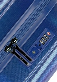 Valigia rigida blu con superficie texturizzata, doppie cerniere nere e un pannello con lucchetto a combinazione sul lato.