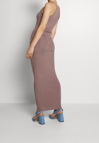 Langes, enges Kleid in Mauve, aus dehnbarem Stoff. Kombiniert mit blauen High-Heelsandalen mit strukturiertem Design und Schnalle.