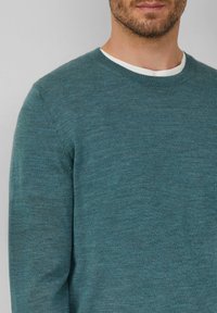 Niebiesko-zielony sweter z okrągłym dekoltem wykonany z miękkiego materiału dzianinowego. Posiada ribbowany dekolt i gładką fakturę, z wszytymi rękawami.